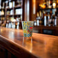 Colorful Portugal souvenir shot glass featuring Barcelos rooster illustrations and classic Portuguese tile patterns on a rustic wooden bar.
