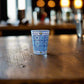 Portugal souvenir shot glass decorated with intricate blue Portuguese azulejo tiles displayed on a wooden bar counter.