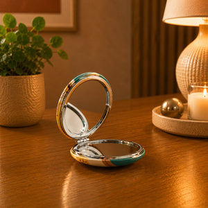 Open Portugal compact travel mirror with vibrant Portuguese landmark artwork, displayed on a wooden surface in a warm indoor setting.