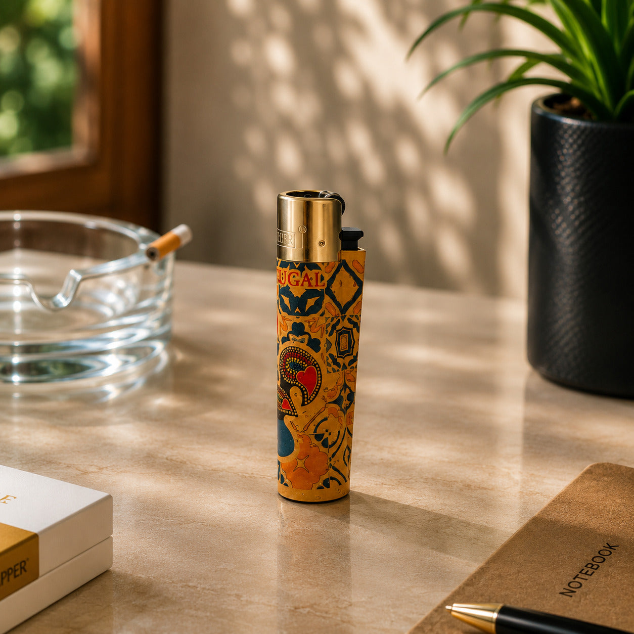 Portugal cork Clipper lighter featuring colourful Barcelos Rooster artwork and traditional Portuguese azulejo patterns displayed on a desk in a warm lifestyle setting with natural light and decorative elements around it.