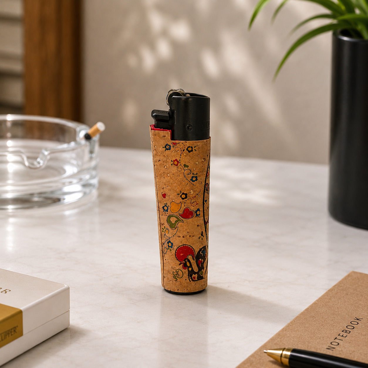 Portugal cork Clipper lighter decorated with a traditional Barcelos Rooster illustration and colourful Portuguese folk art patterns photographed at an angle in a lifestyle setting.