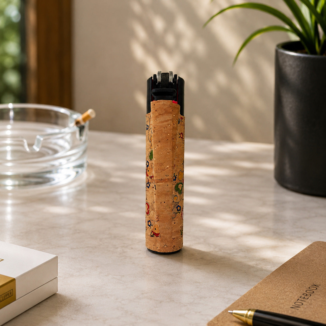 Rear view of a Portugal cork Clipper lighter showcasing the natural cork finish and refillable mechanism in a bright lifestyle setting with decorative desk accessories.