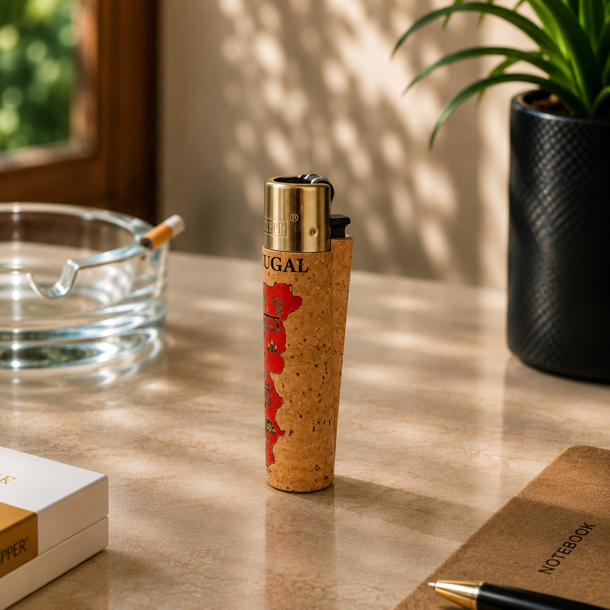 Portugal cork Clipper lighter with Portugal map artwork and regional cultural symbols photographed at an angle in a lifestyle setting with warm sunlight and decorative desk accessories.