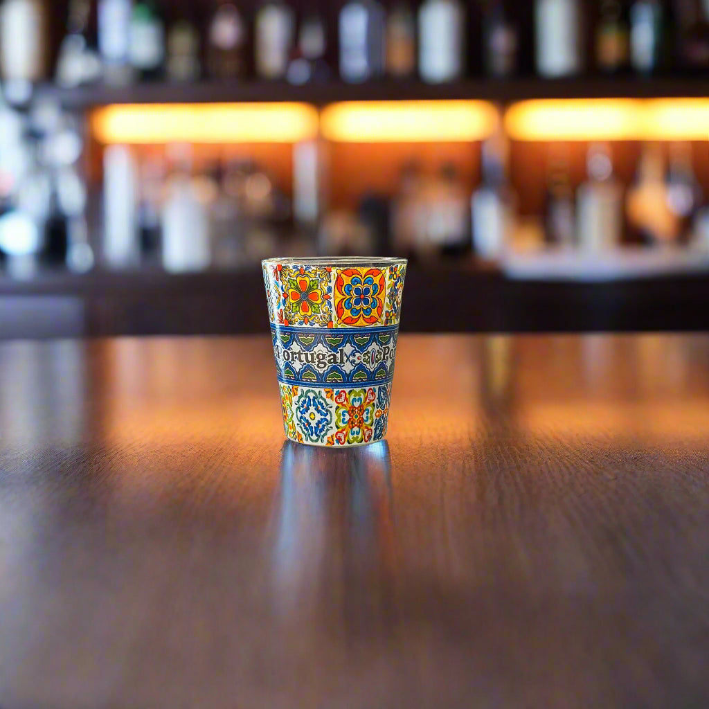 Traditional Portugal souvenir shot glass with colorful azulejo-inspired patterns photographed on a wooden table in a warm bar setting.