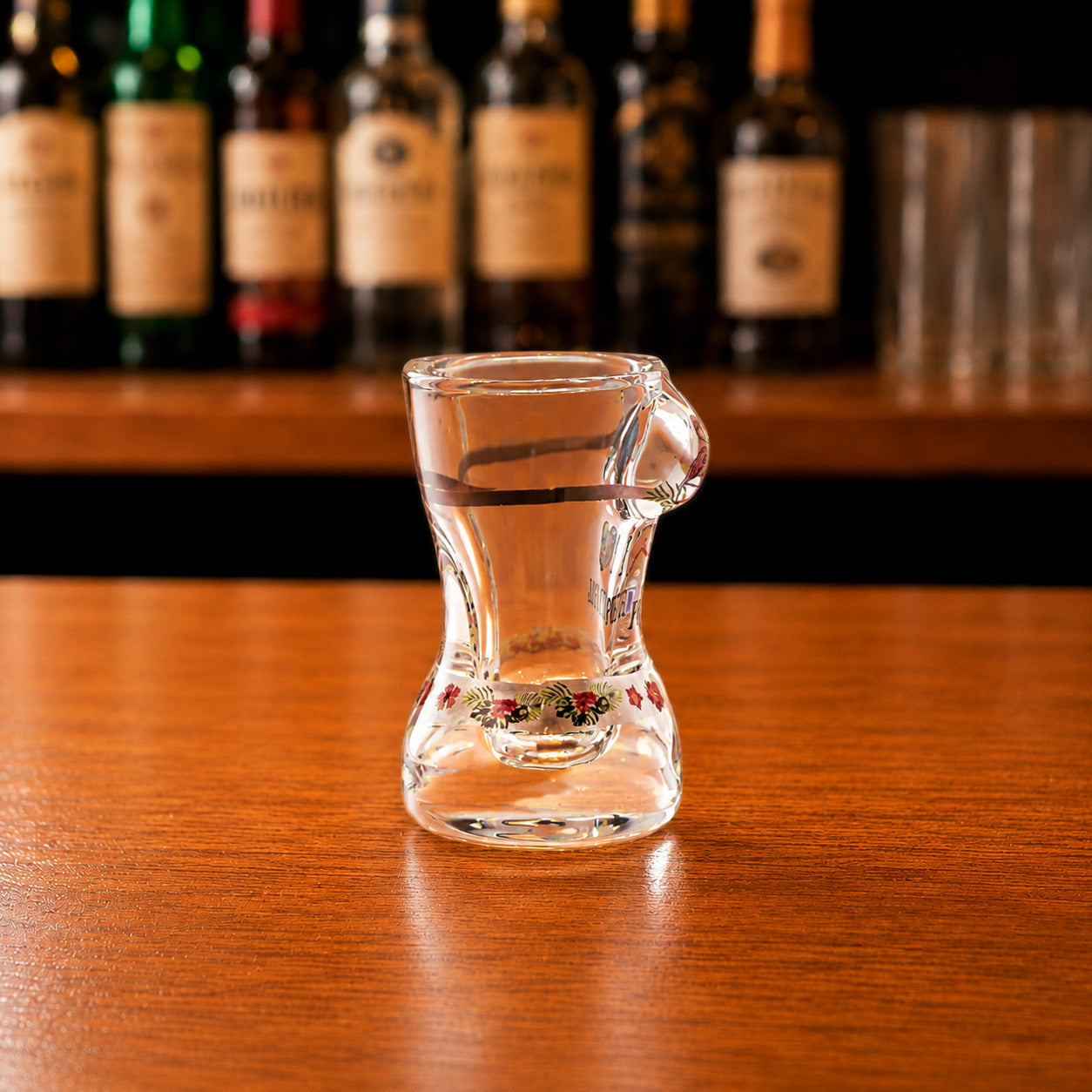 Side profile of Portugal flamingo bikini style shot glass with transparent glass body and floral decorative artwork on wooden bar counter.