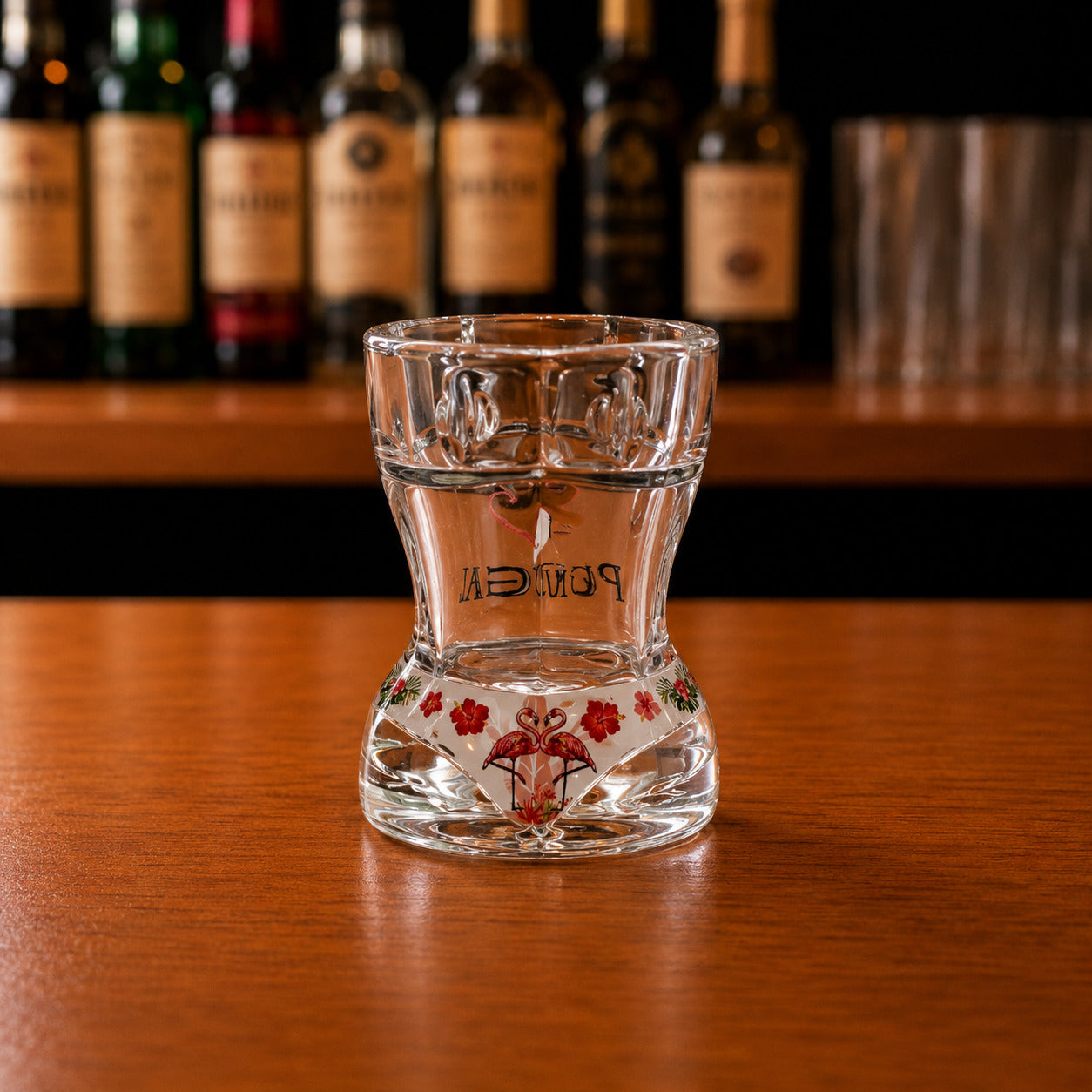 Back view of Portugal flamingo bikini style shot glass with floral tropical artwork displayed on wooden bar surface.