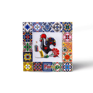 A vibrant square ceramic tile, perfect for souvenirs, featuring a traditional Portuguese rooster in the center, surrounded by intricate floral and geometric patterns. The word "Portugal" graces the bottom, with lively blue, yellow, red, and green colors adorning the border. It's also a handy magnet!