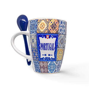 A colorful ceramic coffee mug featuring a mosaic tile design and the word "PORTUGAL" in the center. This souvenir mug is adorned with blue and yellow intricate patterns resembling traditional Portuguese tiles. A small blue ceramic spoon is attached to the handle.