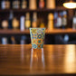 Portugal shot glass decorated with traditional Portuguese azulejo tiles displayed on a wooden bar counter with blurred background.