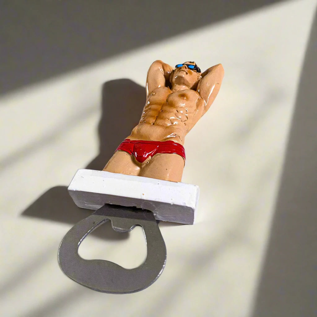 A bottle opener featuring a figurine of a muscular man in red swim briefs and sunglasses, posed with his hands behind his head. This playful "Portugal man" design makes for a distinctive and fun souvenir.