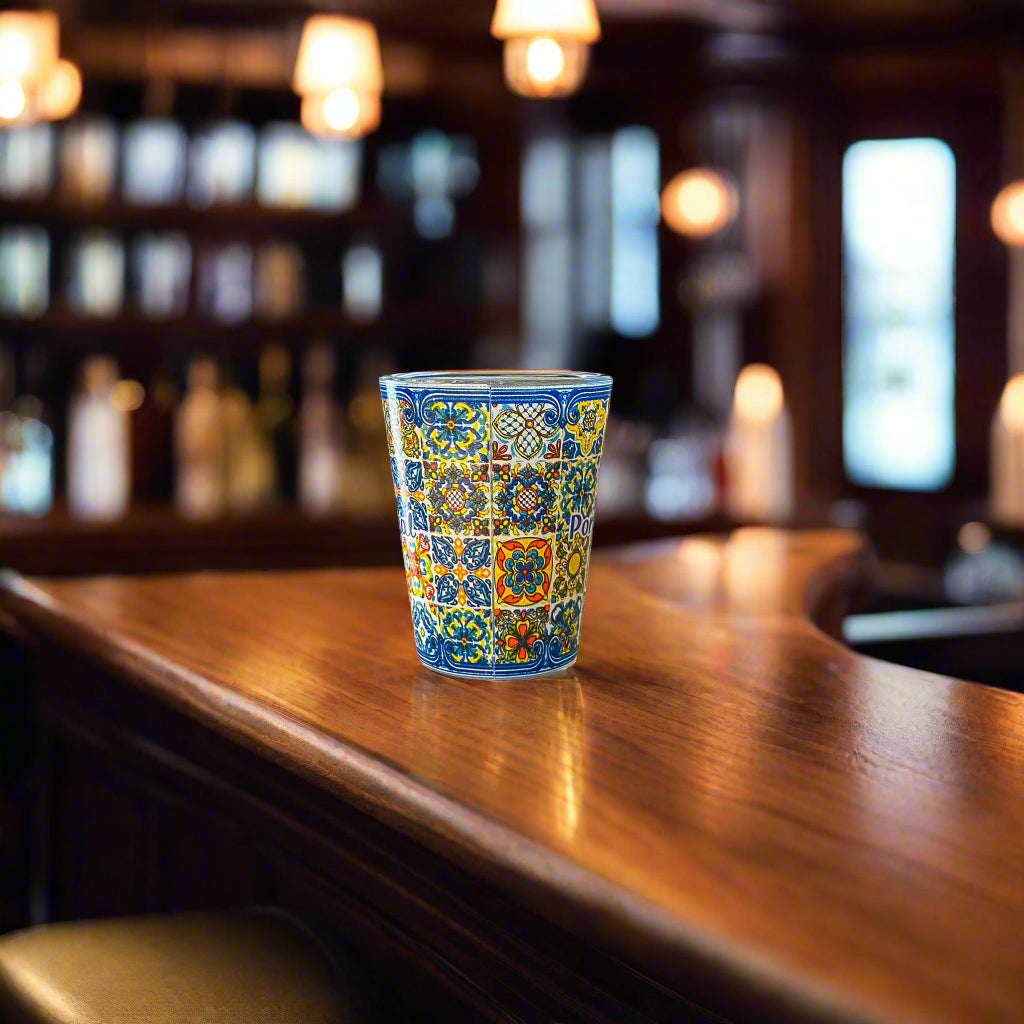 Colorful Portugal shot glass with classic Portuguese azulejo patterns photographed on a wooden bar with blurred background lights.