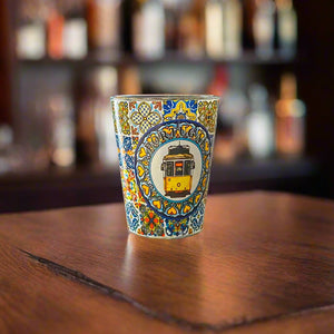 Portugal souvenir shot glass featuring iconic yellow Lisbon tram illustration surrounded by colorful Portuguese azulejo patterns on wooden surface.