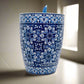 A ceramic souvenir mug decorated with intricate blue and white patterns inspired by traditional Portuguese tiles, with "PORTUGAL" elegantly encircling the base. The mug is paired with a matching blue spoon that slots conveniently into the handle.