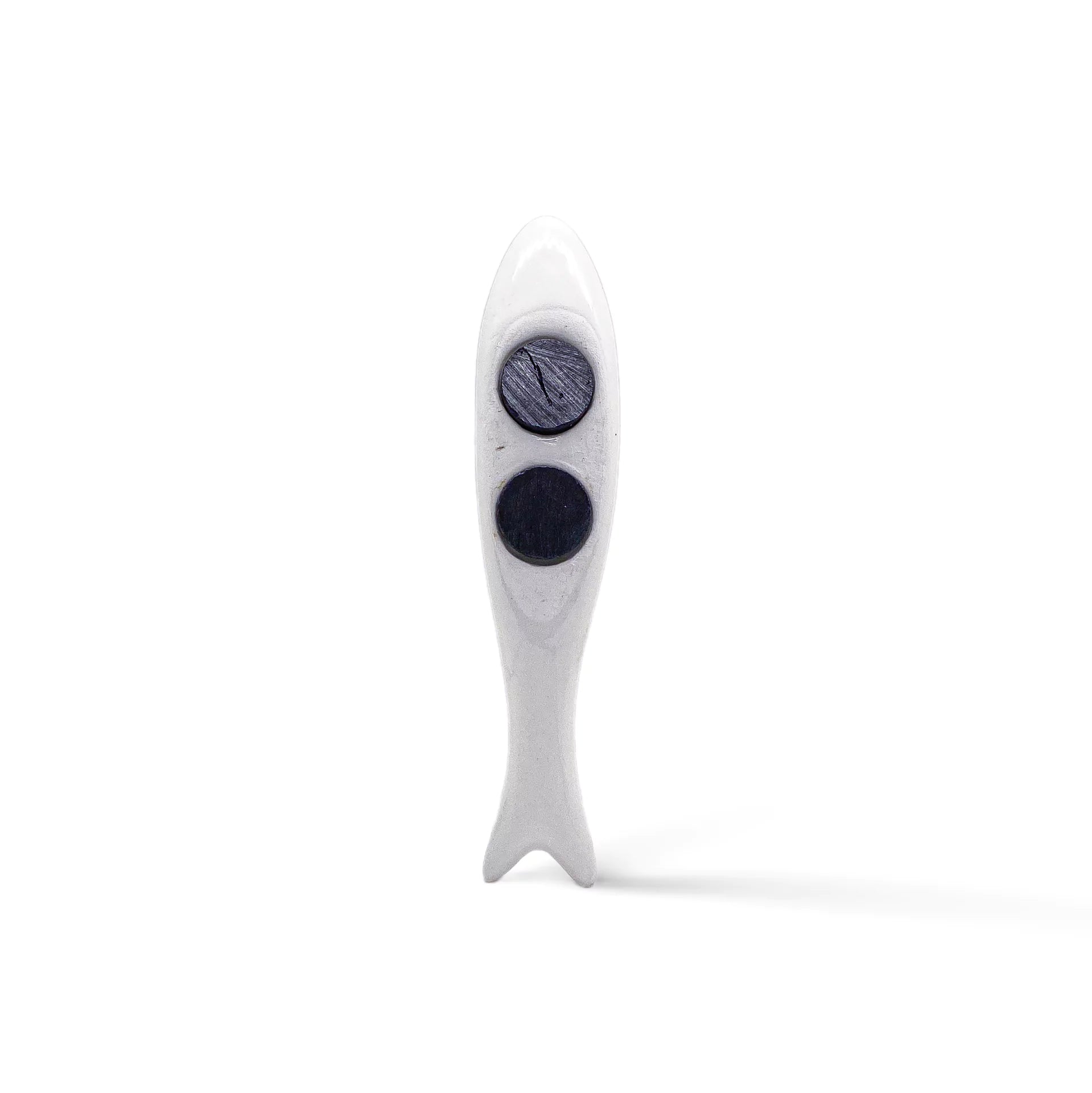 A small, white, sculpted figurine in the shape of a sardine stands upright on a plain white background. The fish has two large, circular, dark indents on its body, resembling eyes. The texture appears smooth with a minimalist design—perfect as a souvenir from Portugal.