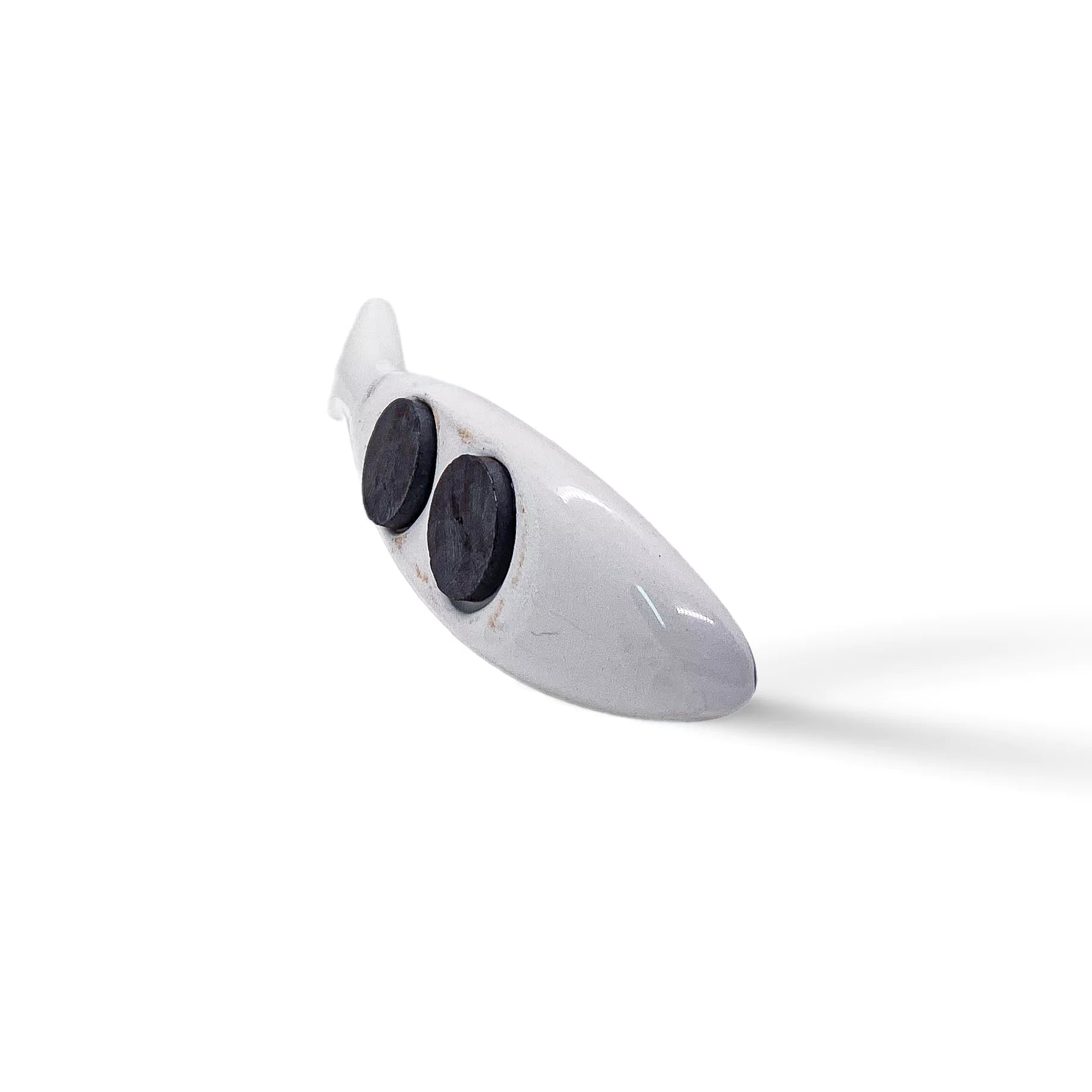 This sleek, white sculpted sardine figurine stands tall on a simple white backdrop. Its minimalist design is highlighted by two large, dark circular indents representing eyes, and a smooth texture. A perfect, contemporary souvenir from Portugal.