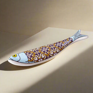 A stylized fish sculpture, inspired by the iconic Portuguese sardine, showcases a blue head and a body adorned with intricate patterns in yellow, white, and purple. The fish has a prominent yellow eye and a light blue tail that subtly blends into the background, making this vibrant piece a striking magnet as well as a beautiful decorative item.