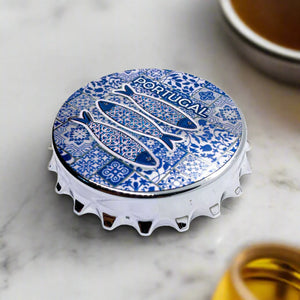 A bottle cap design featuring three fish with intricate patterns set against a blue and white tiled background, reminiscent of traditional Portuguese tiles. The word "Portugal" is prominently placed above the fish, while the cap's classic crimped edges add a touch of authenticity. It also doubles as a magnet, blending functionality with style.