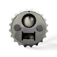 A close-up image of a mechanical part resembling a gear or cogwheel with a circular shape and multiple small teeth around the edge. The gear features three distinct circular compartments and a rectangular slot, giving it a face-like appearance, much like a quirky magnet from Portugal.
