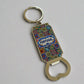A keychain bottle opener adorned with a vibrant tile pattern and "Portugal" prominently displayed in the center. The intricate design blends geometric and floral elements in bright, lively colors. This practical souvenir features a circular keyring at the top and a sturdy metal opener at the bottom, combining functionality with a touch of Portuguese charm.