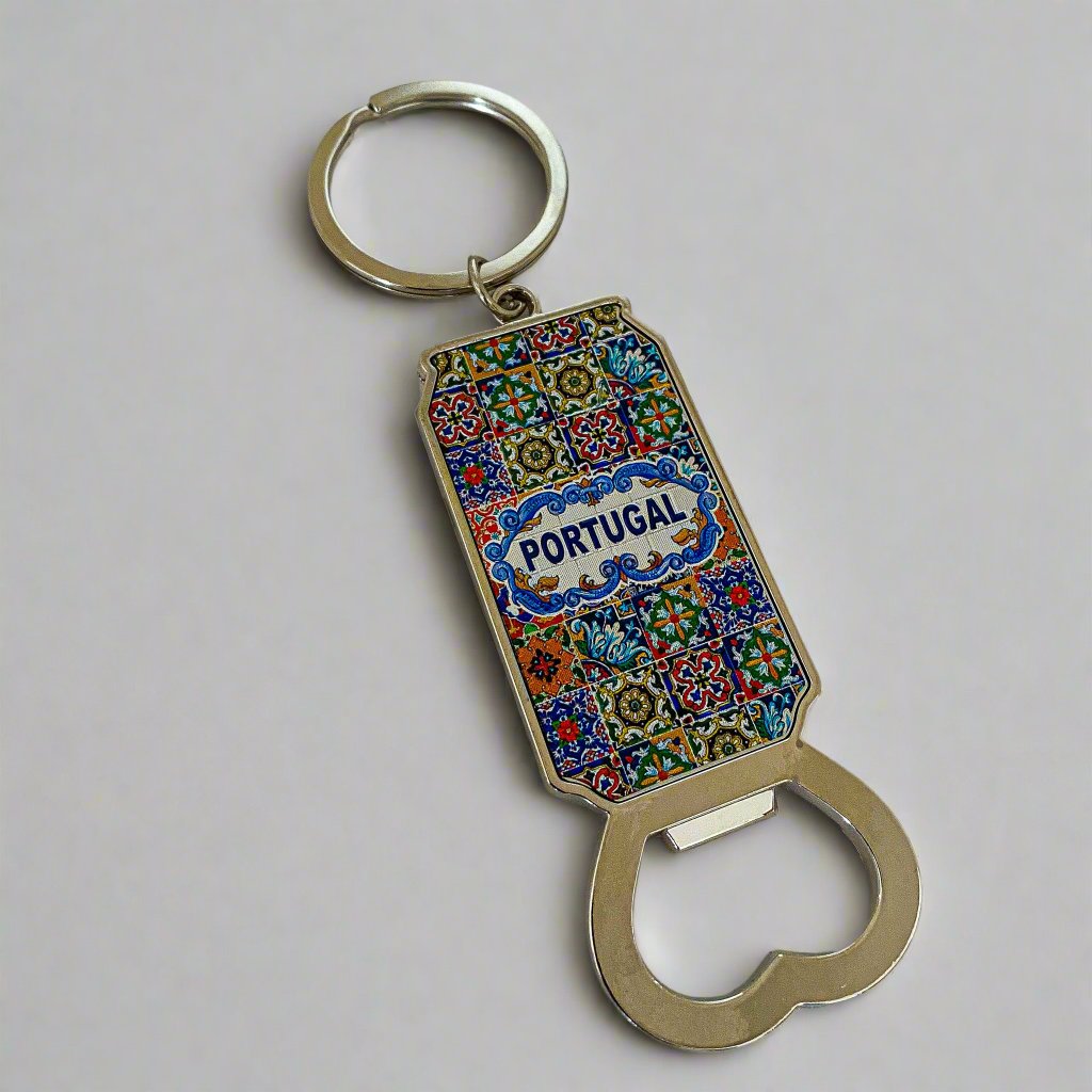 A keychain bottle opener adorned with a vibrant tile pattern and "Portugal" prominently displayed in the center. The intricate design blends geometric and floral elements in bright, lively colors. This practical souvenir features a circular keyring at the top and a sturdy metal opener at the bottom, combining functionality with a touch of Portuguese charm.
