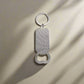 Keychain bottle opener with a rectangular silver body and a circular keyring at the top, casting a shadow on a light beige surface. Perfect for adding a touch of Portugal to your everyday essentials.