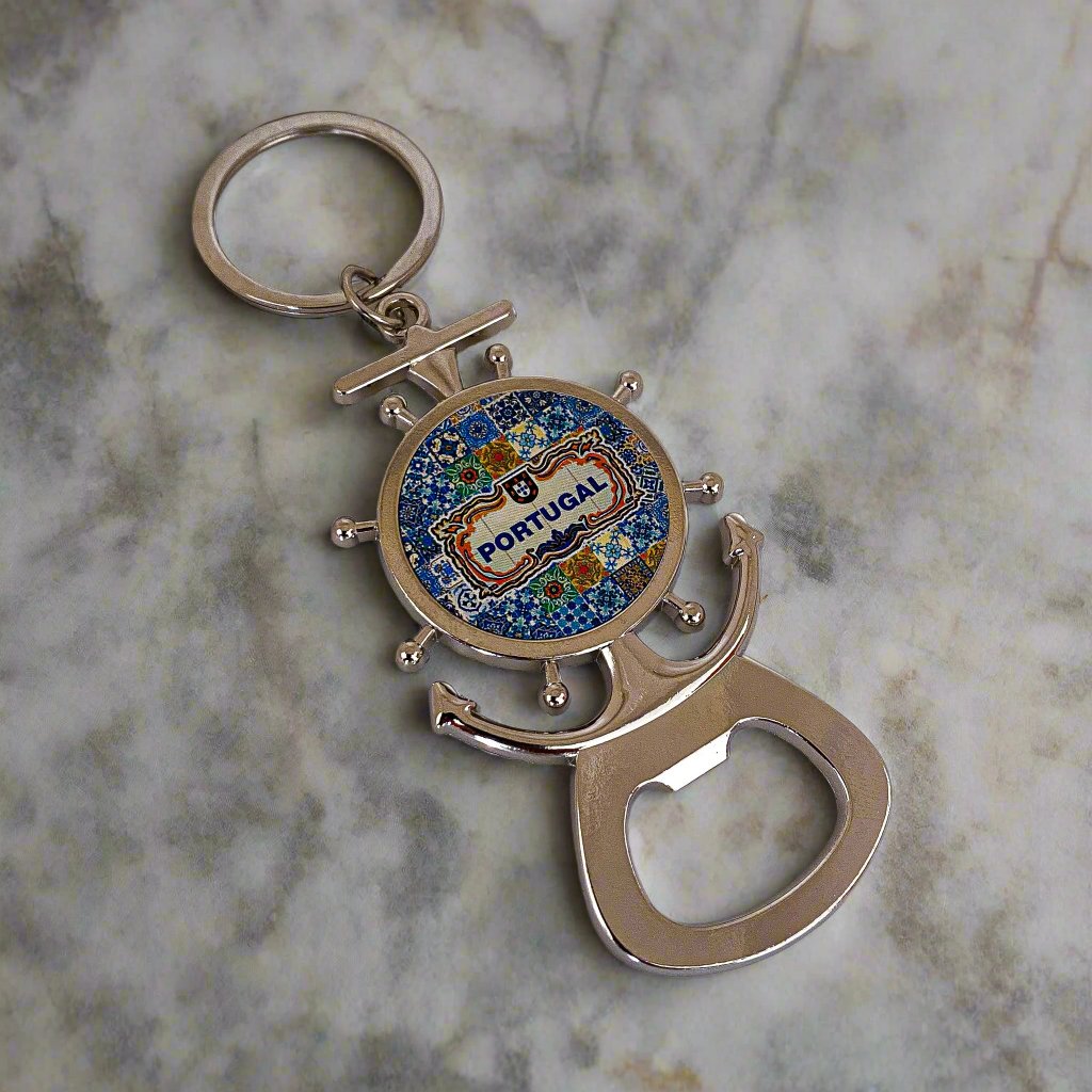 A metal keychain shaped like a ship's wheel and anchor, featuring a vibrant design in the center with the word "Portugal." The keychain includes a bottle opener at the base and a magnet on the back, combining functionality with a nautical-themed souvenir charm.