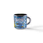 A small blue and white metal shot glass, perfect as a souvenir, is decorated with intricate patterns depicting traditional Portuguese tiles. The word "Portugal" is written centrally among the designs. The cup has a handle on the right side and casts a slight shadow.