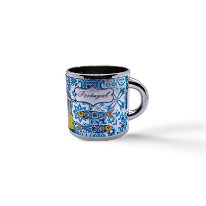 A small blue and white metal shot glass, perfect as a souvenir, is decorated with intricate patterns depicting traditional Portuguese tiles. The word "Portugal" is written centrally among the designs. The cup has a handle on the right side and casts a slight shadow.