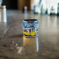 A small blue and white metal shot glass, ideal as a souvenir, featuring intricate patterns inspired by traditional Portuguese tiles. The word "Portugal" is prominently displayed at the center of the design. The shot glass includes a handle on the right side and casts a subtle shadow, adding depth to its elegant look.