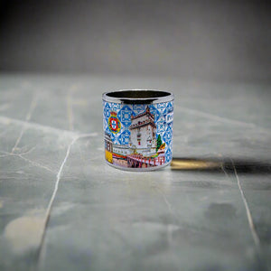 A small metal mug showcases the word "Portugal" against a blue and white tile-inspired pattern, reminiscent of traditional Portuguese azulejos. The design is accented by vibrant illustrations, including the iconic Portuguese rooster, making it a charming addition alongside your favorite Portugal-themed magnets.