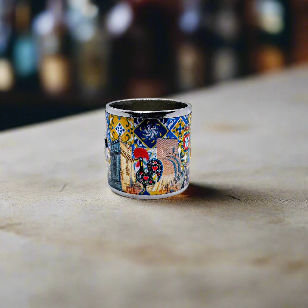 A vibrant ceramic mug adorned with intricate artwork showcasing iconic scenes from Portugal. The design features traditional motifs, famous landmarks, and a crest, with the word "Portugal" boldly displayed in the center. The handle and rim are finished in metallic silver, adding an elegant touch to this perfect souvenir.