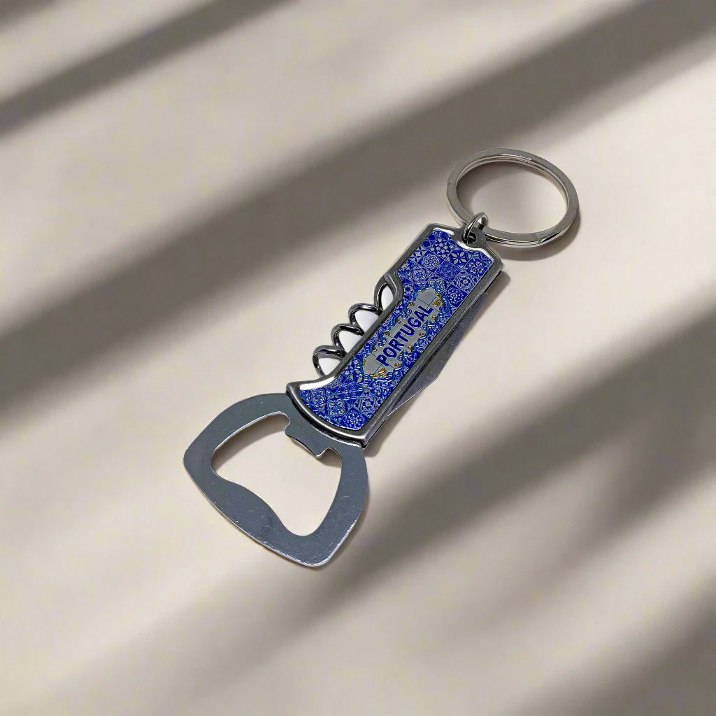A blue and silver souvenir keychain that includes a bottle opener, a corkscrew, and a small knife. The keychain features an intricate blue design and is attached to a metal ring. The background is plain white.