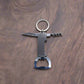 A multi-functional keychain against a wooden background. This souvenir from Portugal features a small knife blade, a corkscrew, and a bottle opener, all made of metal. The keyring is attached to the top of the tool.