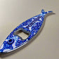 A fish-shaped bottle opener with vibrant, intricate metal patterns and "PORTUGAL" written in blue on the body. This practical souvenir doubles as a magnet, ideal for displaying on your fridge as a memento of Portugal.