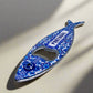 A metal bottle opener shaped like a fish, featuring vibrant, intricate patterns. The word "PORTUGAL" is boldly displayed in blue on the sardine’s body. This versatile souvenir also functions as a magnet, perfect for displaying on your fridge.