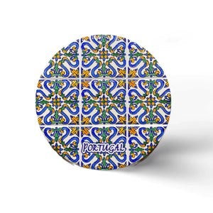 A round cork coaster displays a colorful, intricate tile pattern featuring blue, yellow, and green designs. The word "Portugal" is written near the bottom in a decorative font. The background is white and minimalistic. This charming item makes for a perfect souvenir from Portugal.