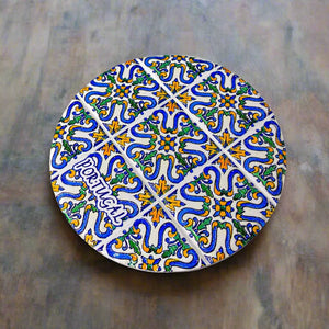 A circular cork coaster showcases a vibrant tile pattern with intricate blue, yellow, and green designs. The word "Portugal" is elegantly written at the bottom in a decorative font. Set against a clean white background, this charming souvenir captures the essence of Portuguese artistry.