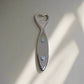 This fish-shaped metal bottle opener showcases elaborate blue and white designs that echo Portuguese azulejos tiles. "Portugal" is prominently featured on its side, and a magnet on the back enables it to adhere to your refrigerator. The opener is positioned at the fish's tail end.