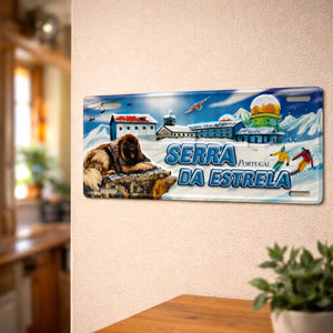 Serra da Estrela metal souvenir sign mounted on a wall featuring snowy mountains, a mountain dog, ski activity and alpine buildings