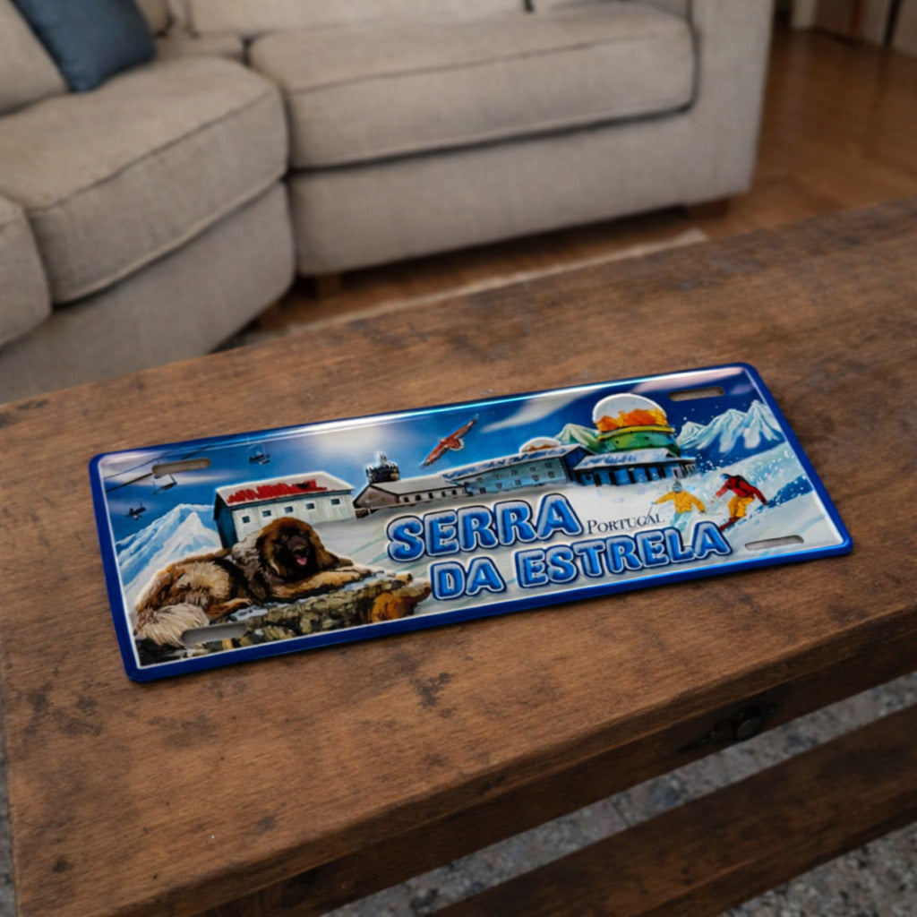 Serra da Estrela metal souvenir sign placed on a wooden table showing snow landscape, mountain dog and winter sports scene