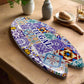 An oval ceramic piece showcasing a vibrant mosaic pattern inspired by traditional Portuguese azulejo tiles. At its center, "PORTUGAL" is written in bold blue uppercase letters. The souvenir rests on a cork base, casting a subtle shadow against the white background.