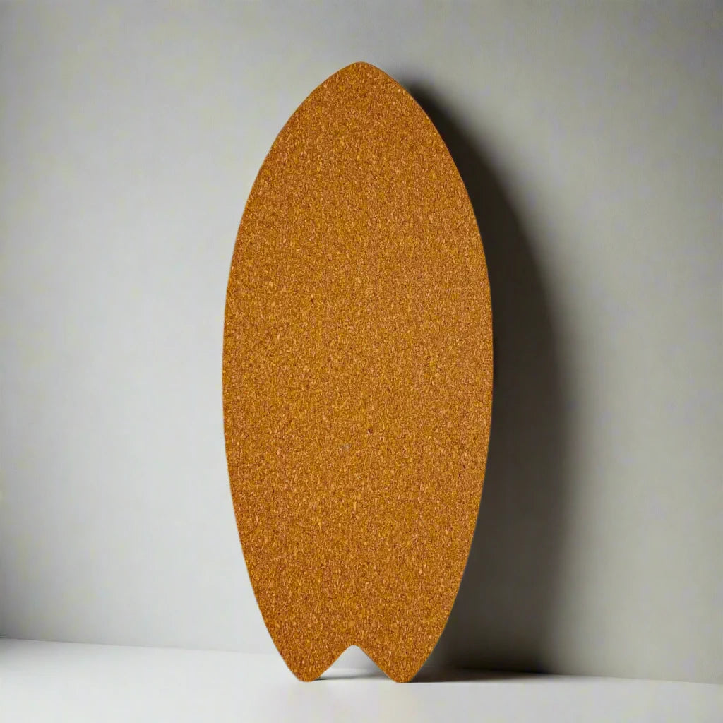 A surfboard-shaped cork board mounted on a wall with the word "PORTUGAL" printed in black letters in the bottom right corner, serving as a charming souvenir. Subtle shadows fall across the wall and board, suggesting natural light from a nearby window.