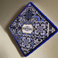 This square-shaped ceramic tile features an intricate blue and white design, with "Portugal" in the middle. Framed with a blue braided cord, the tile also has a cork base for extra sturdiness and comes with a loop for hanging.
