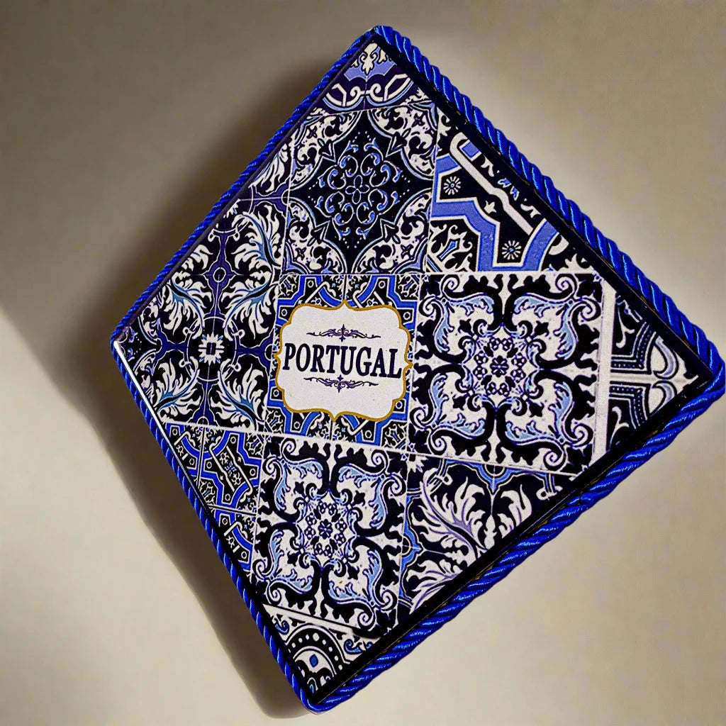 This square-shaped ceramic tile features an intricate blue and white design, with "Portugal" in the middle. Framed with a blue braided cord, the tile also has a cork base for extra sturdiness and comes with a loop for hanging.