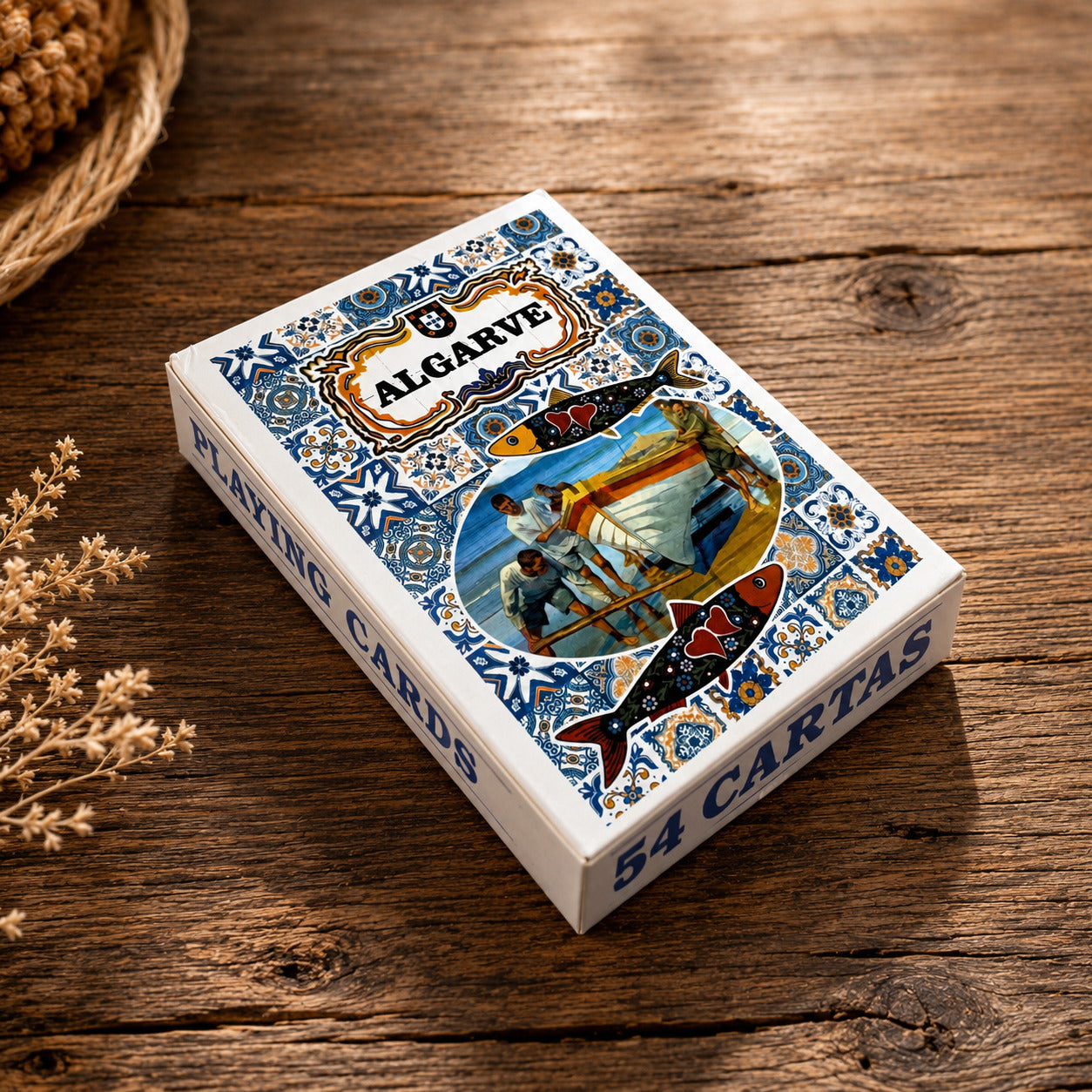 Algarve Portugal souvenir playing card box on a wooden table, featuring blue azulejo tiles, decorative sardines, and a traditional fishing boat scene.