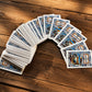 Algarve souvenir playing cards spread on a rustic wooden table, showing an azulejo-inspired back design with sardines and traditional Portuguese fishing artwork.