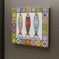 Decorative tile with three fish illustrations and a colorful border on a gray background