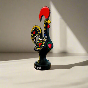 A black rooster figurine embellished with red and yellow feathers, representing the iconic Galo de Barcelos from Portugal.