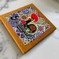 Cork coaster with colorful design featuring a rooster and text on a marble surface
