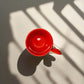 Red ceramic cup with white handle on a light gray surface